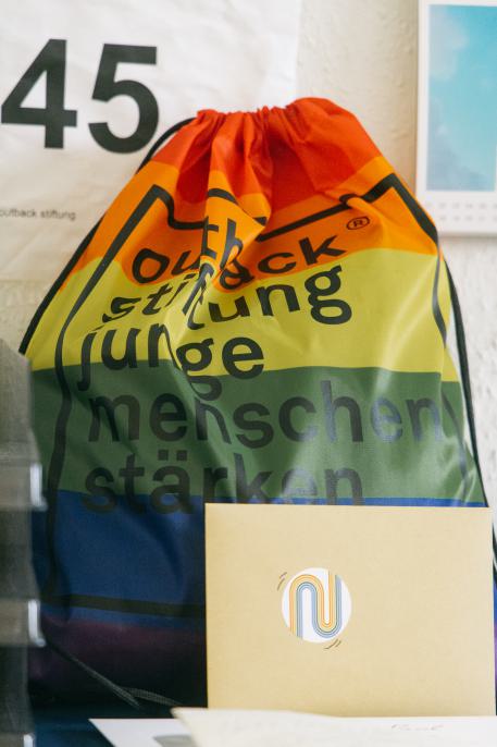 Unterstützung für LSBTI*  Kinder, Jugendliche und ihre Familien Beutel in Regenbogenfarben und dem Outback-Logo