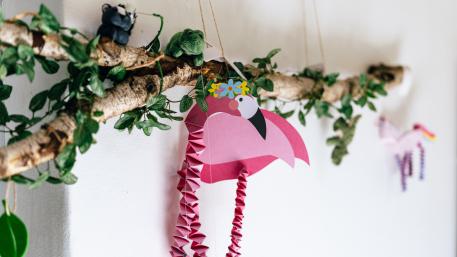 Pflegefamilien in der Jugendhilfe ein Ast mit Efeu, daran hängt ein gebastelter pinker Flamingo
